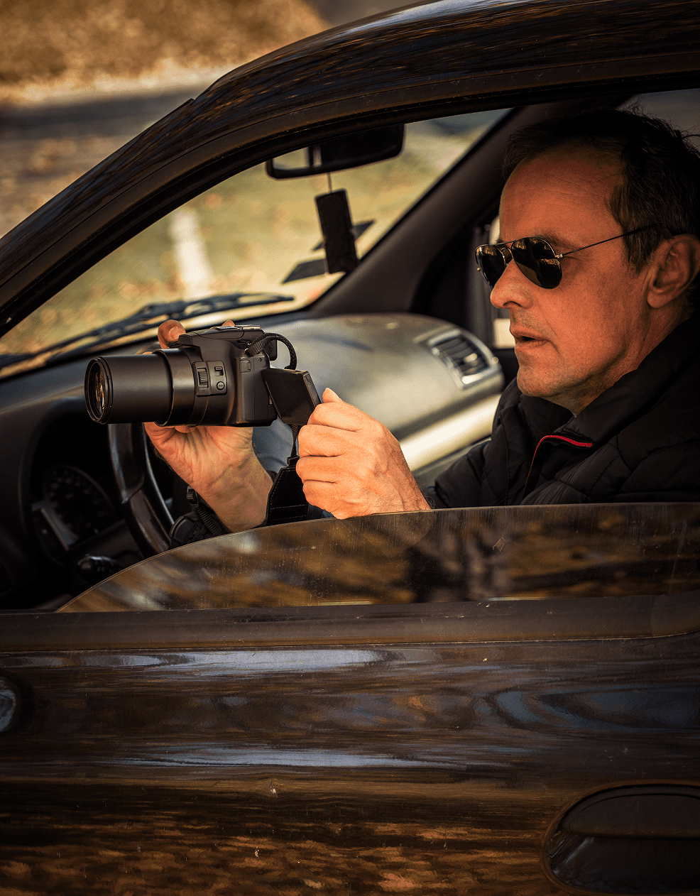 Man in car holding a camera.